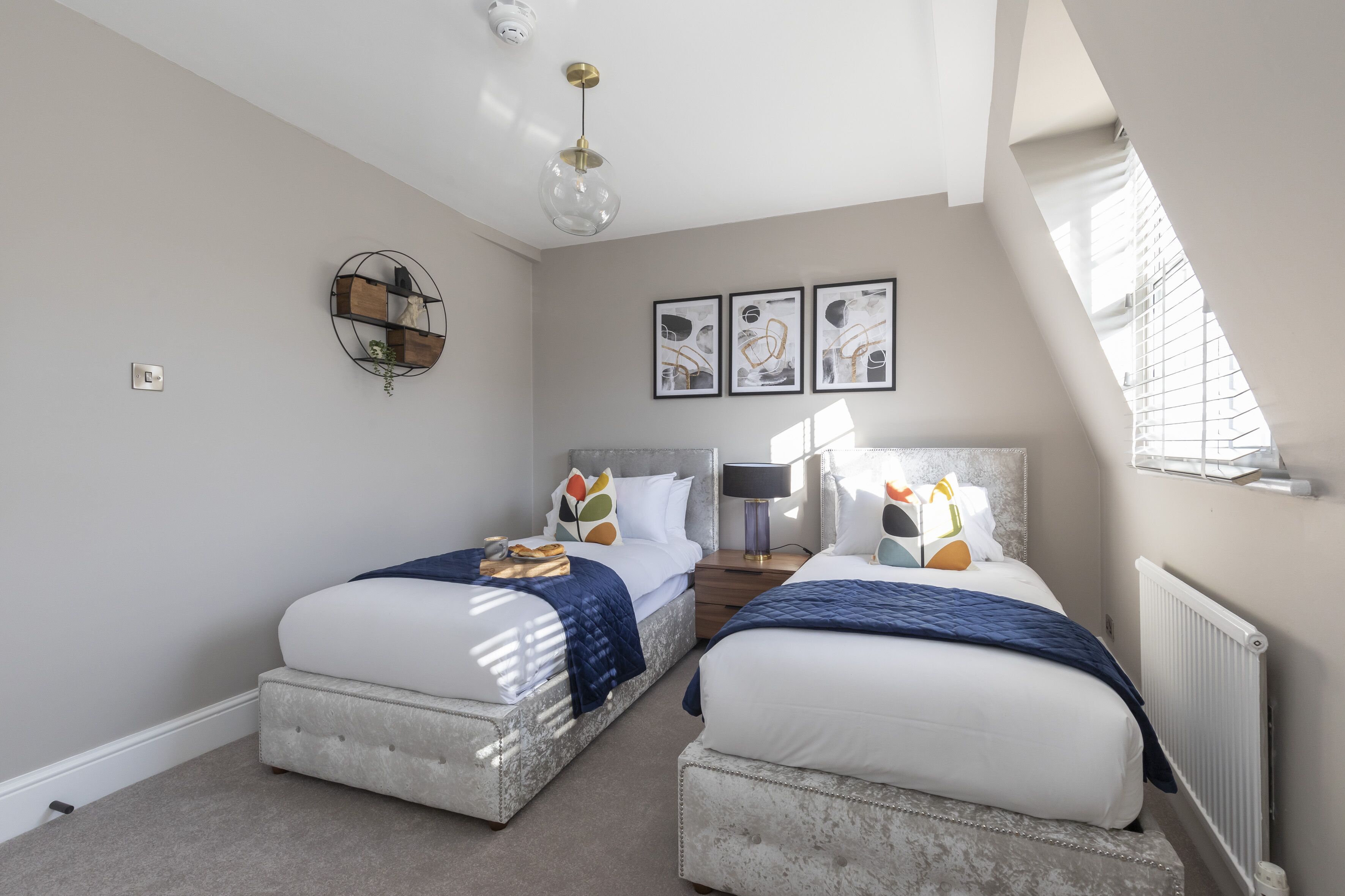 Een slaapkamer met twee bedden, een plafondlamp, een wandplank en lijstwerken.