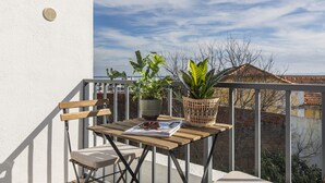 Een balkon met een houten tafel, twee stoelen, een tijdschrift en twee planten in potten.