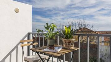 A balcony with a wooden table, two chairs, a magazine, and two potted plants.