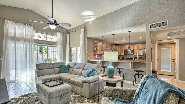A spacious living area with a sectional sofa, ottoman, and a patterned rug. There is a ceiling fan, a kitchen area with bar stools, and a door leading to another room. - Near Golf! Snowbird Poolside Escape in Scottsdale (Scottsdale)