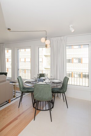 A dining area with a round table, green chairs, and a chandelier.