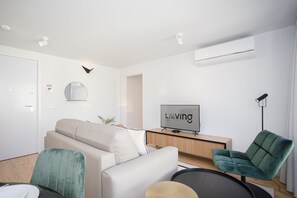 A modern living room with a sofa, a green chair, a TV, and a desk.