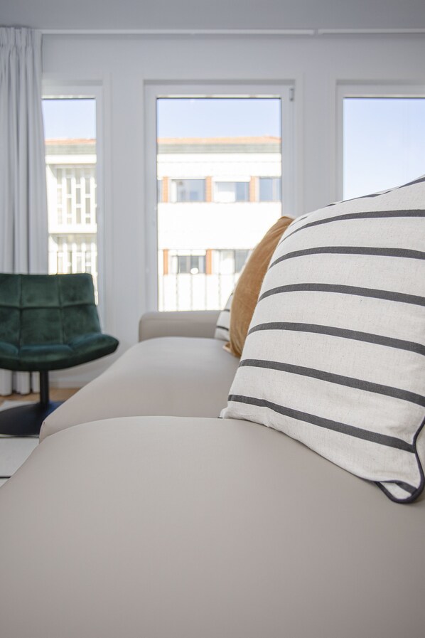 A room with a sofa, a green chair, and a window with a view of buildings.