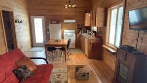 A cozy cabin interior with a red sofa, wooden dining table, kitchen area, and a fireplace. - Cozy Suite 15 min away from Mt Tremblant. Pet Friendly (Mont-Tremblant)