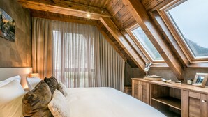 Ein Schlafzimmer mit einem großen Bett, Holzbalken an der Decke, einem Fenster und einem Schreibtisch mit verschiedenen Gegenständen.