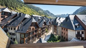 Eine Reihe traditioneller Chalets mit steilen Dächern und Holzbalkonen, vor einer Berglandschaft mit bewaldeten Hängen.