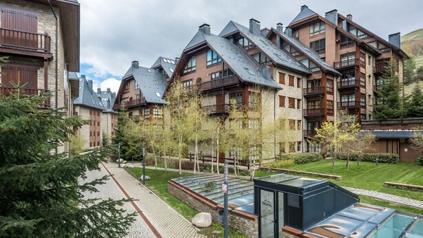 Un hotel moderno con varias construcciones, una piscina cubierta por una estructura de vidrio y un jardín bien cuidado.