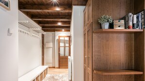Un pasillo con vigas de madera, un banco blanco, un radiador y una estantería con libros y una planta.