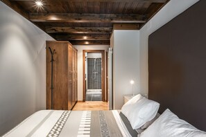 Una camera da letto con soffitto in legno, un letto con copriletto decorato, un comodino con lampada e una porta che dà su un bagno con doccia.