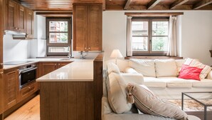Una cocina moderna con armarios de madera y una isla grande, un área de estar acogedora con un sofá y una mesita de centro, y una ventana con cortinas.