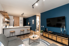 Un salón moderno con un sofá gris, una mesa de centro redonda y un televisor en una pared azul.