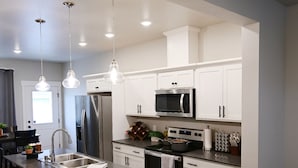 A modern kitchen with stainless steel appliances, white cabinetry, and pendant lighting. - Cozy townhome (Billings)