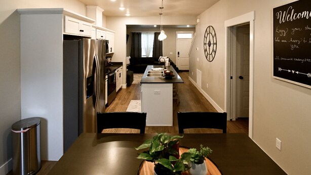 A modern kitchen with a central island, stainless steel appliances, and a dining area with a table and chairs. - Cozy townhome (Billings)