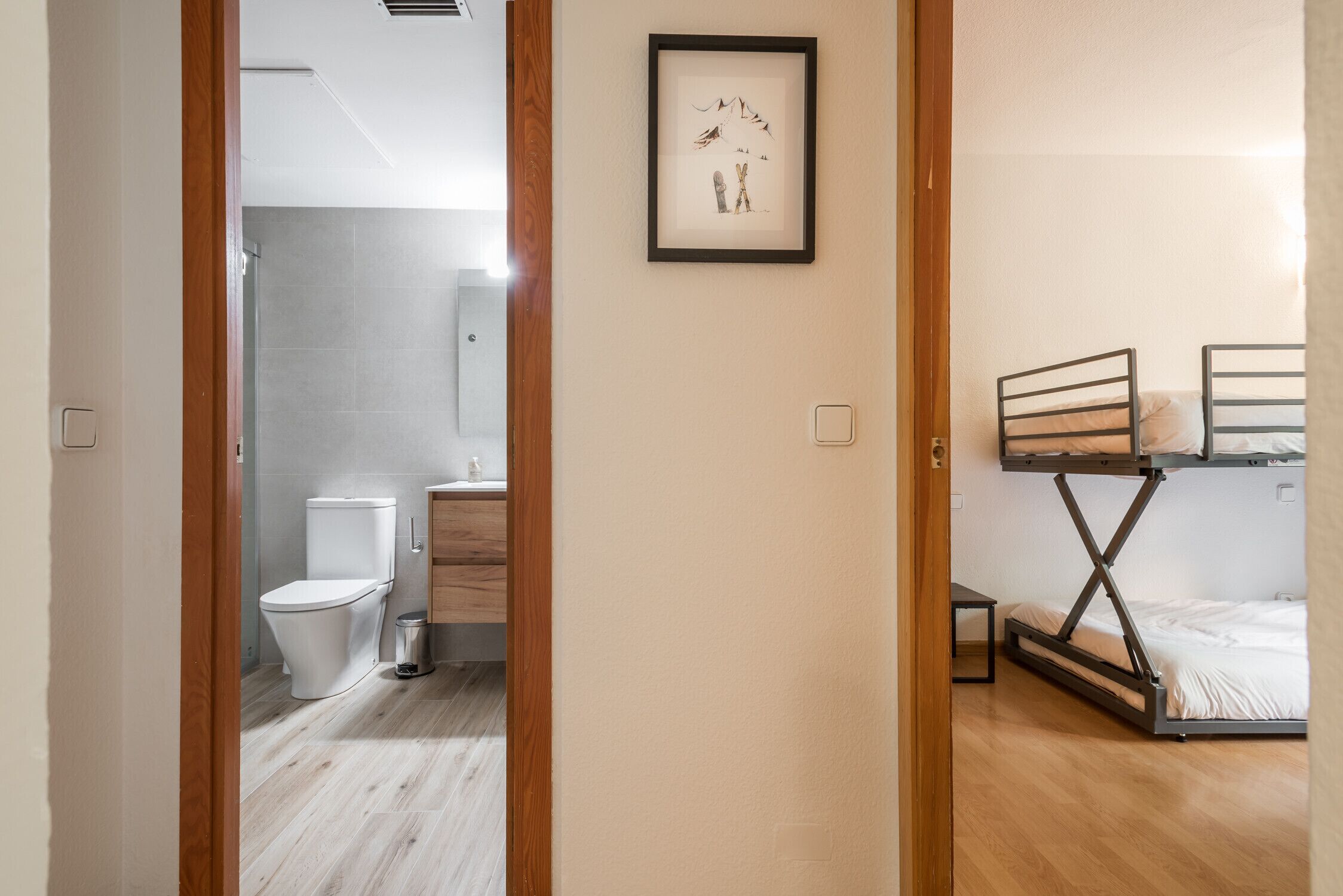 Een kamer met een houten vloer, een bed met metalen frame, een klein tafeltje en een ingelijste foto aan de muur.