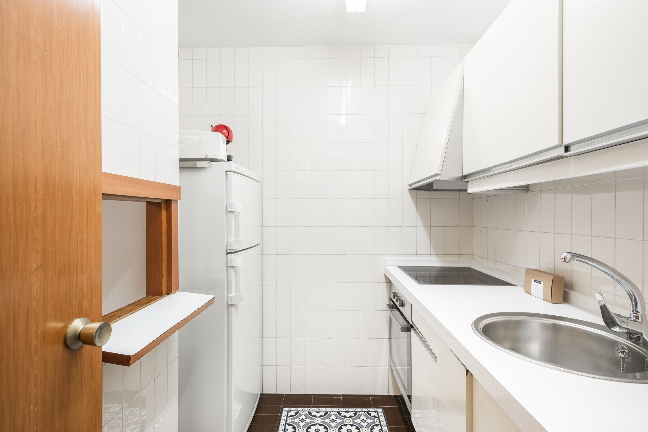 Une cuisine de taille réduite avec des meubles blancs, un évier en acier inoxydable et un carrelage décoratif.