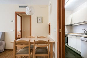 Een compacte keuken met witte kastjes, een houten eettafel en een hangende lamp.