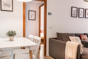 Een moderne woonkamer met een witte eettafel, een bruine bank en kunstwerken in lijsten aan de muren.
