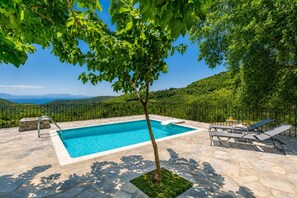Una piscina con plataforma de piedra, un árbol y vistas a las colinas.
