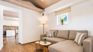 Una sala de estar moderna con un sofá, dos mesitas, una lámpara y una ventana con una planta.