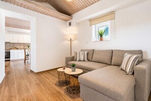 Una sala de estar moderna con un sofá, dos mesitas, una lámpara y una ventana con una planta.