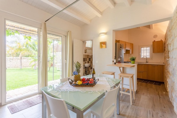 Une cuisine moderne avec des meubles en bois, un coin repas doté d’une table en verre et une vue sur un jardin grâce à de grandes fenêtres.