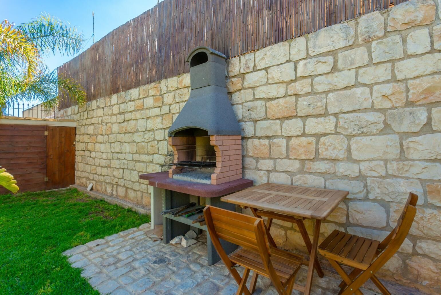 An outdoor brick oven with a table and chairs, set against a stone wall.