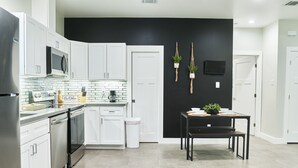 A modern kitchen with white cabinets, a black wall, and a dining area with a table and chairs.