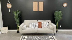 A living room with a grey sofa, patterned cushions, a black and white rug, and two wooden wall decorations.