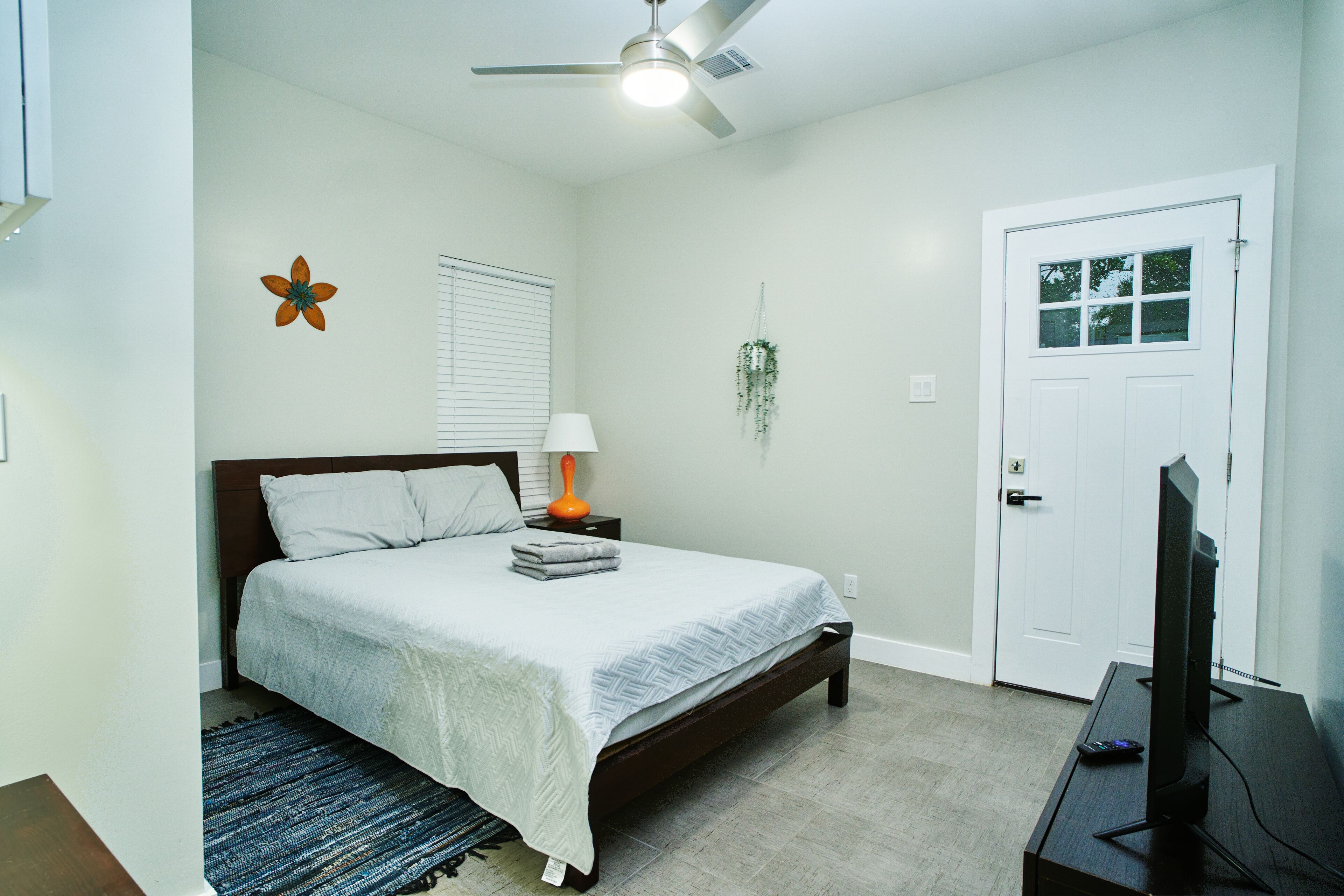 A bedroom with a bed, a ceiling fan, a television, and a door.