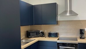 Moderni keittiö, jossa on tummat kaapit, mikroaaltouuni, leivänpaahdin, kahvinkeitin ja sisäänrakennettu uuni.