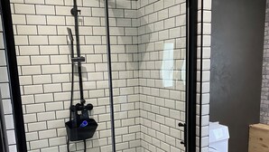 Moderni suihkukaappi, jossa on lasiovi, musta runko ja laatoitettu seinä.