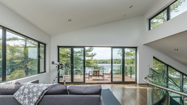 A modern interior with a large sofa, a telescope, and a balcony with outdoor furniture. - Cherry Island Muskokas Premiere Private Island (Utterson)