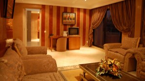 A living room with striped wallpaper, a television, a sofa, a chair, and a coffee table with a floral arrangement. - Mounia (Fes)