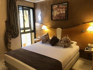 Hotelkamer met een bed, twee nachtkastjes, een lamp, een schilderij aan de muur en een raam met gordijnen.