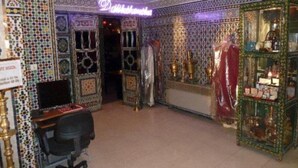 A room with intricate tile work, a desk with a computer, and a display case with items. - Mounia (Fes)