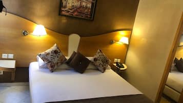 A hotel room with a large bed, two bedside lamps, a painting on the wall, and a small table with a chair.