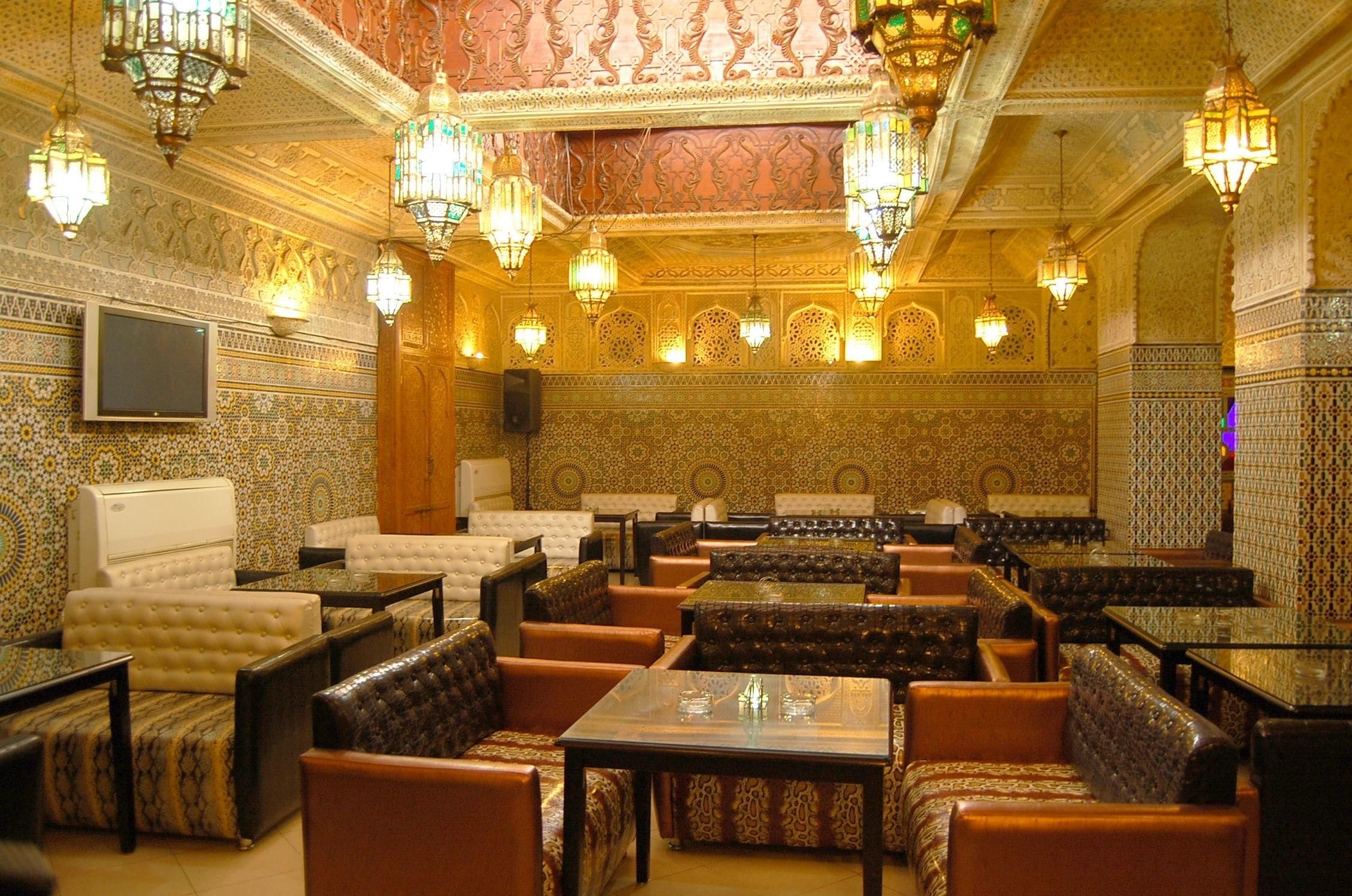 A traditional Moroccan interior with ornate tile work, patterned cushions, and hanging lanterns.