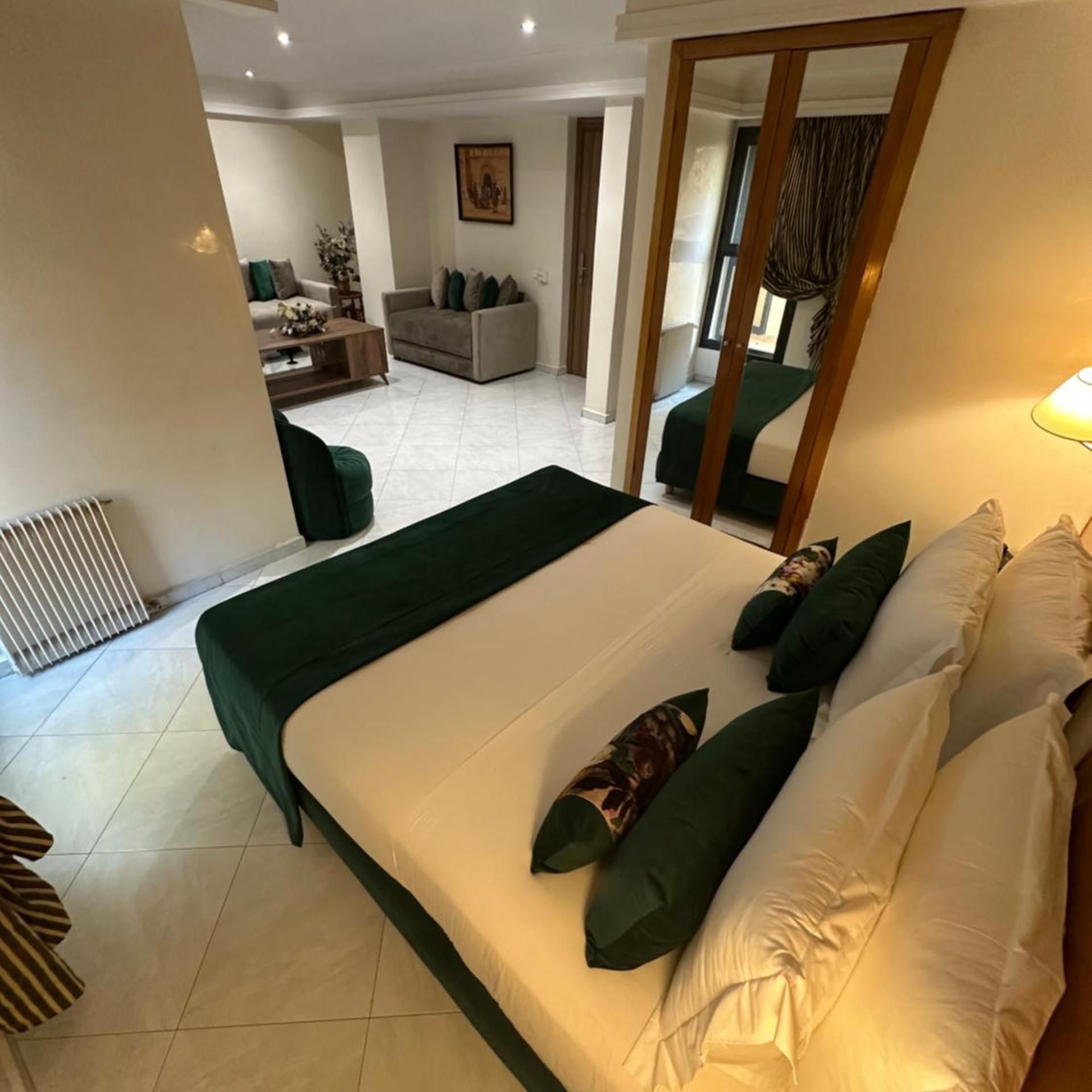 Habitación de hotel con una cama grande, un área de descanso con sofá y sillones, y vista al salón.