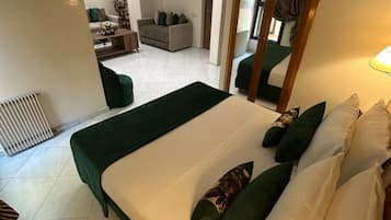 Habitación de hotel con una cama grande, un área de descanso con sofá y sillones, y vista al salón.