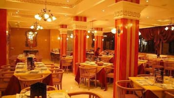 A restaurant with multiple tables and chairs, red and white striped columns, and hanging light fixtures.