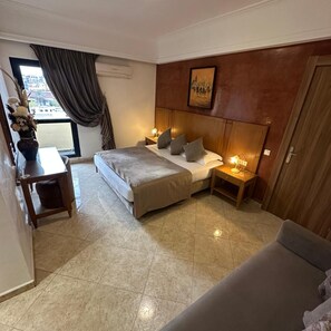 Habitación de hotel con cama, mesitas de noche, escritorio, silla, ventana con cortinas y un cuadro en la pared.