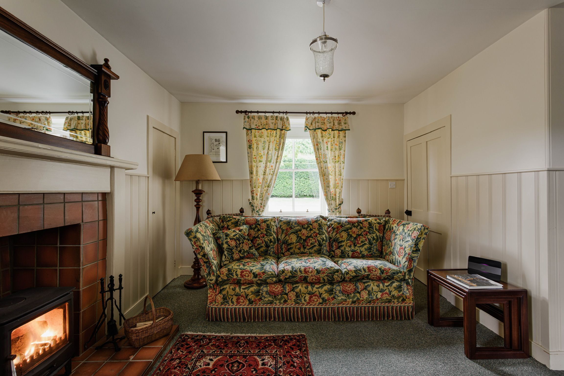 A cozy living room with a fireplace, floral sofa, and a small table.