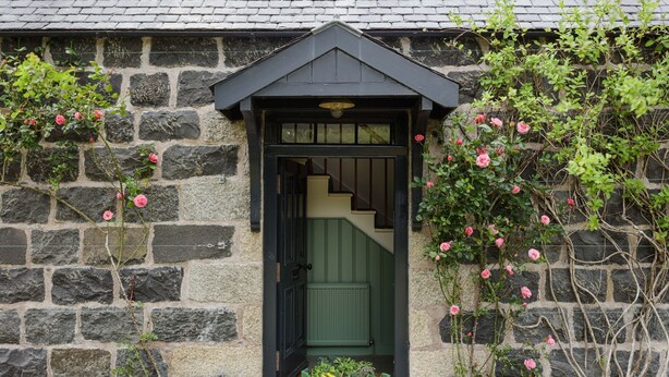 Un bâtiment en pierre avec une porte verte et un petit jardin agrémenté de fleurs roses.