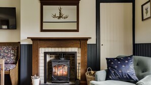 A cozy living room with a fireplace, a sofa, a chair, and a television. - Chic Traditional Highland Estate Cottage with Valley View and Hot Tub (Rothiemay)