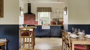 A kitchen with a brick stove, wooden chairs, a dining table set with plates and glasses, and a window with a view of greenery. - Chic Traditional Highland Estate Cottage with Valley View and Hot Tub (Rothiemay)