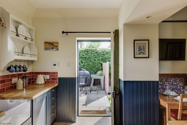 A kitchen with a wooden countertop, built-in cabinets, and a view of an outdoor patio with a grill.