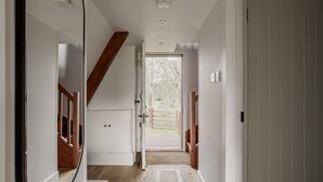 Un pasillo con escalera de madera, paredes blancas y una puerta que da al exterior.