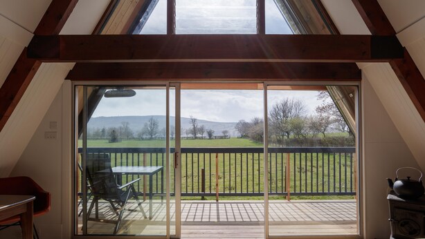 Una habitación con un gran ventanal corredero que da a una terraza exterior con vistas a un campo y colinas.