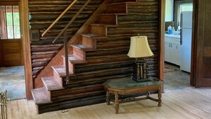 Eine Holztreppe führt zu einer zweiten Etage, ein kleiner Tisch mit einer Lampe und ein durch eine offene Tür sichtbarer Küchenbereich.