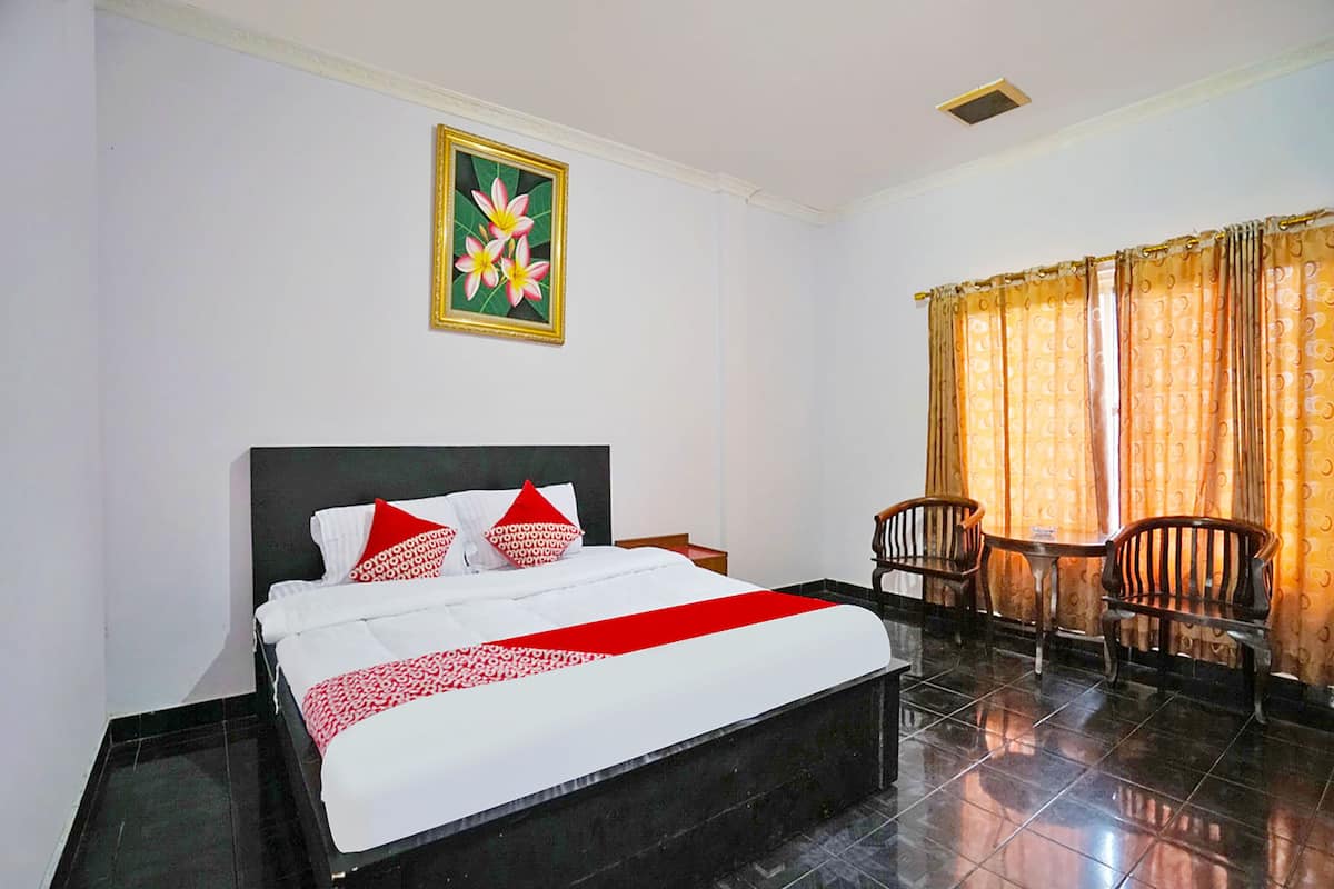 Quarto de hotel com uma cama, uma mesinha, duas cadeiras, uma janela com cortinas e um quadro na parede.